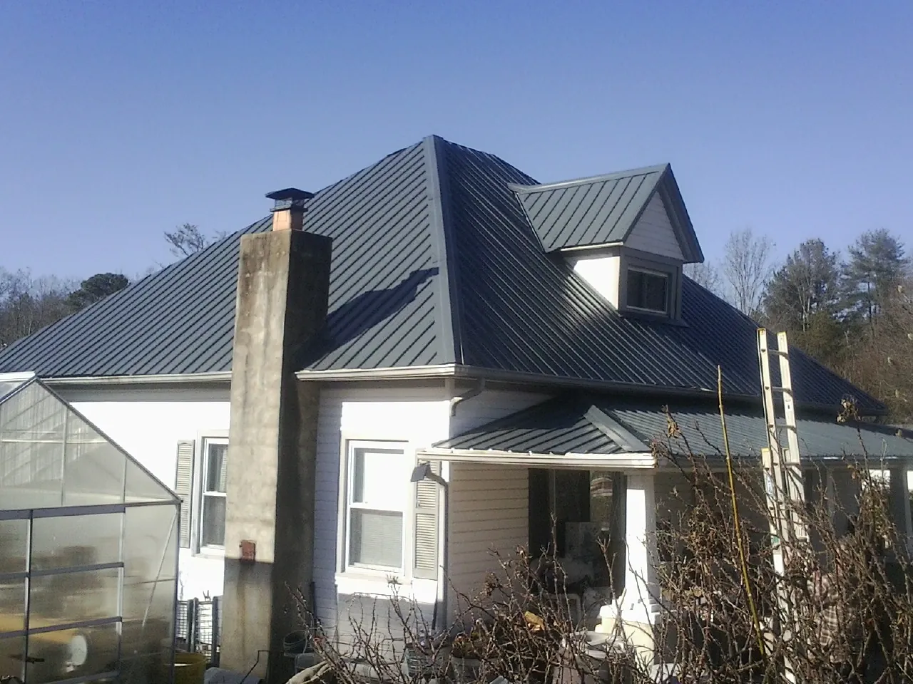 Dark blue standing seam metal roof on a white farmhouse with dormer — Slate & Tile Roof Repair by Roofing Brothers in Taopi
