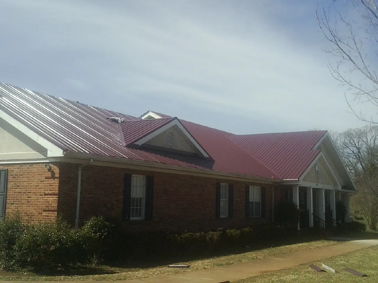 Red metal roof with gabled entries on a long brick building, from a Hail Damage Roof Repair job in Taopi