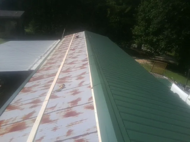 Old rusted panels beside newly installed green metal roofing — Wind Damage Roof Repair by Roofing Brothers in Taopi