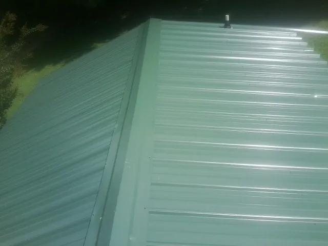 New green metal panels meeting at the ridge of a roof — Flat Roof Repair work by our crew in Taopi