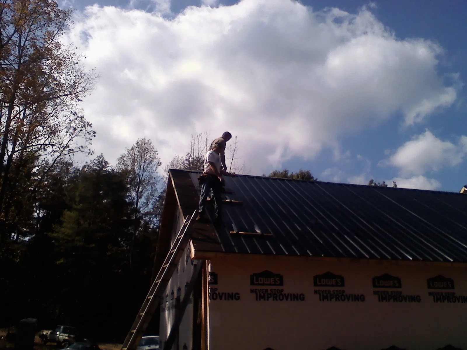 Roofer fastening dark metal panels high against a cloudy sky, from a Roof Inspection job in Taopi