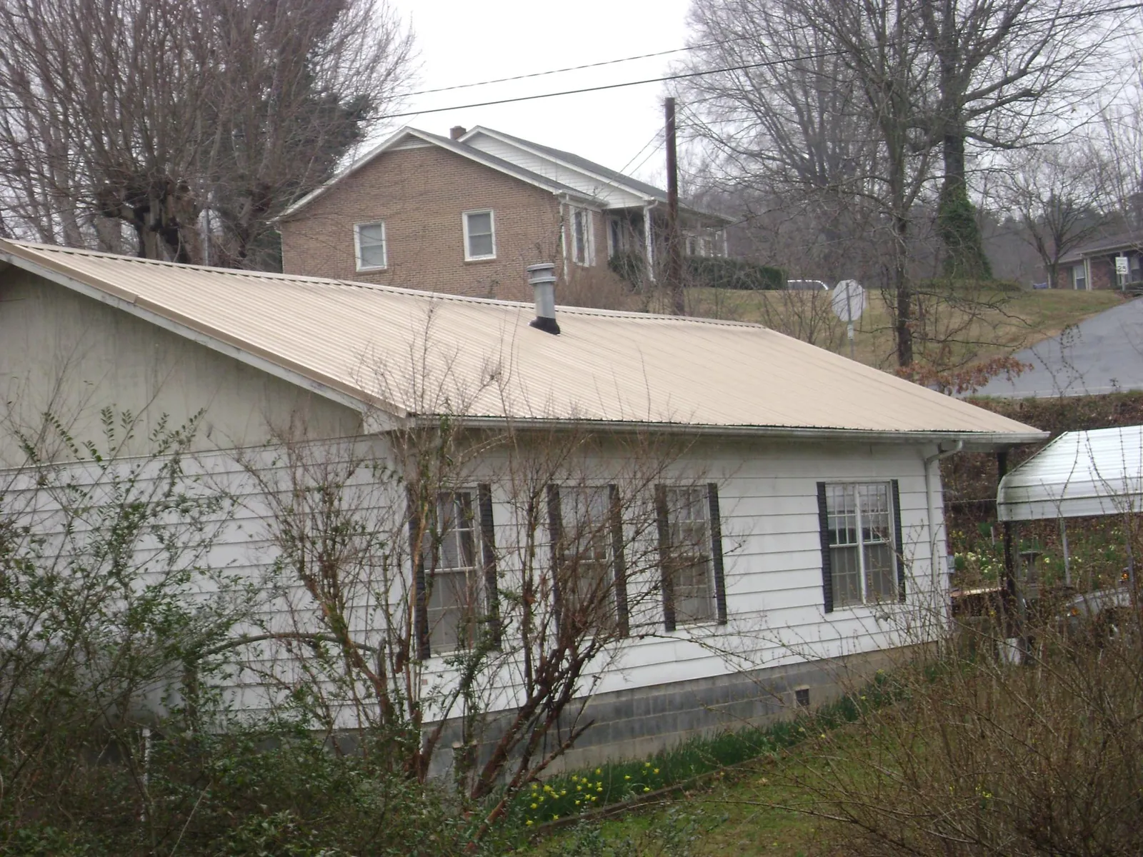 Tan metal roof on a white sided house set into a hillside — Commercial Roofing by Roofing Brothers in Taopi