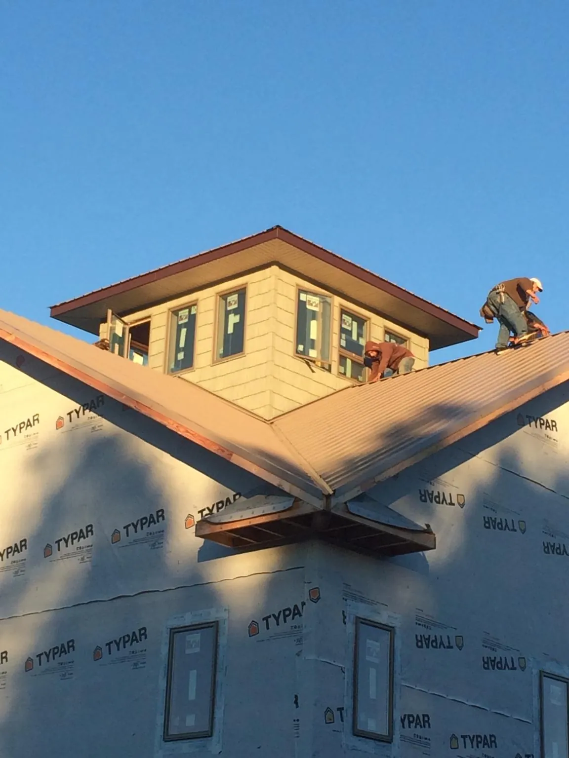 Roofers working around a rooftop cupola on a new metal roof at sunset — Roof Waterproofing in Taopi by Roofing Brothers